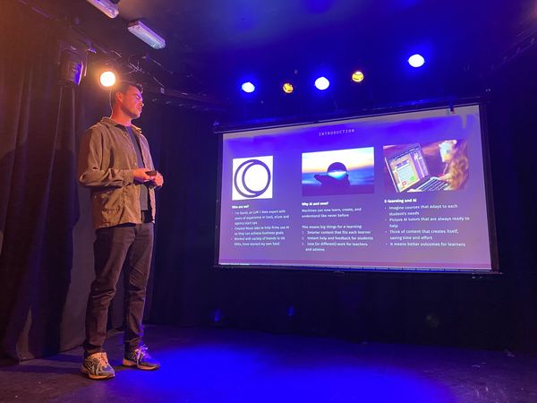 David Stubbs on a small stage under blue and amber lights, holding a clicker, beside a projected slide with the Moon Labs logo.